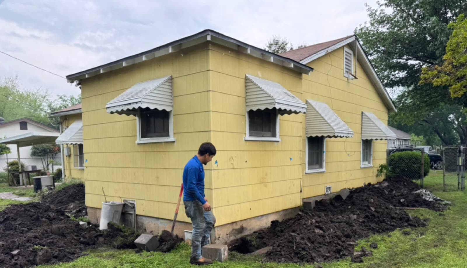 Crew member digging along the foundation of a yellow single story home in Irving during a pier and beam lift